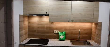 Une cuisine équipée d’un évier à deux bacs, de meubles en bois et d’un sac vert posé sur le plan de travail.