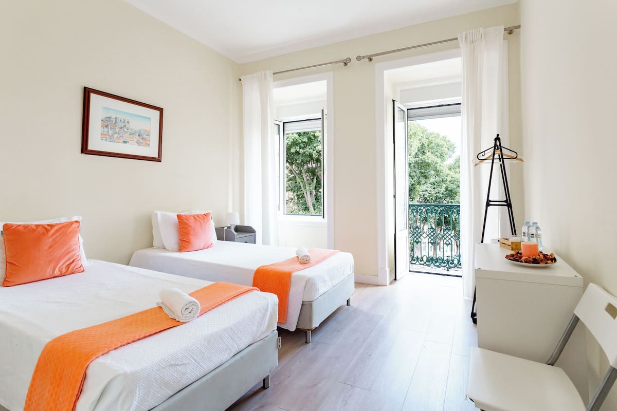 Habitación de hotel con dos camas, un balcón y una mesita con una bandeja de desayuno.