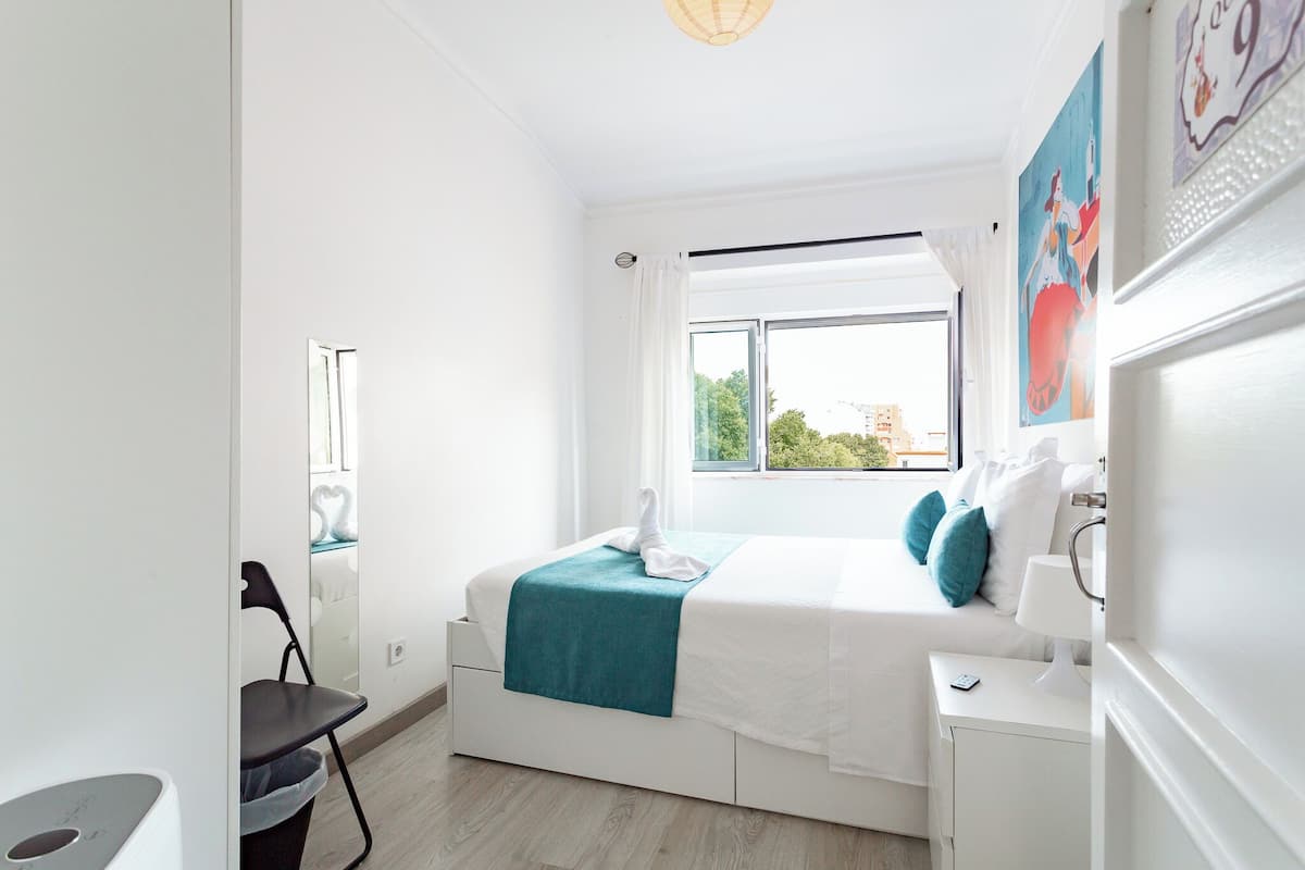 Un dormitorio moderno con cama, mesita de noche, silla y ventana con cortinas.