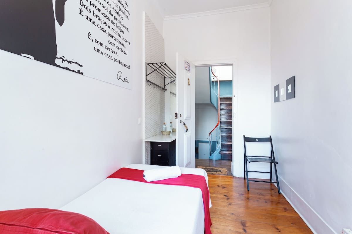 Un dormitorio con una cama, un escritorio y una silla. Se ve una escalera que conduce a otra habitación.