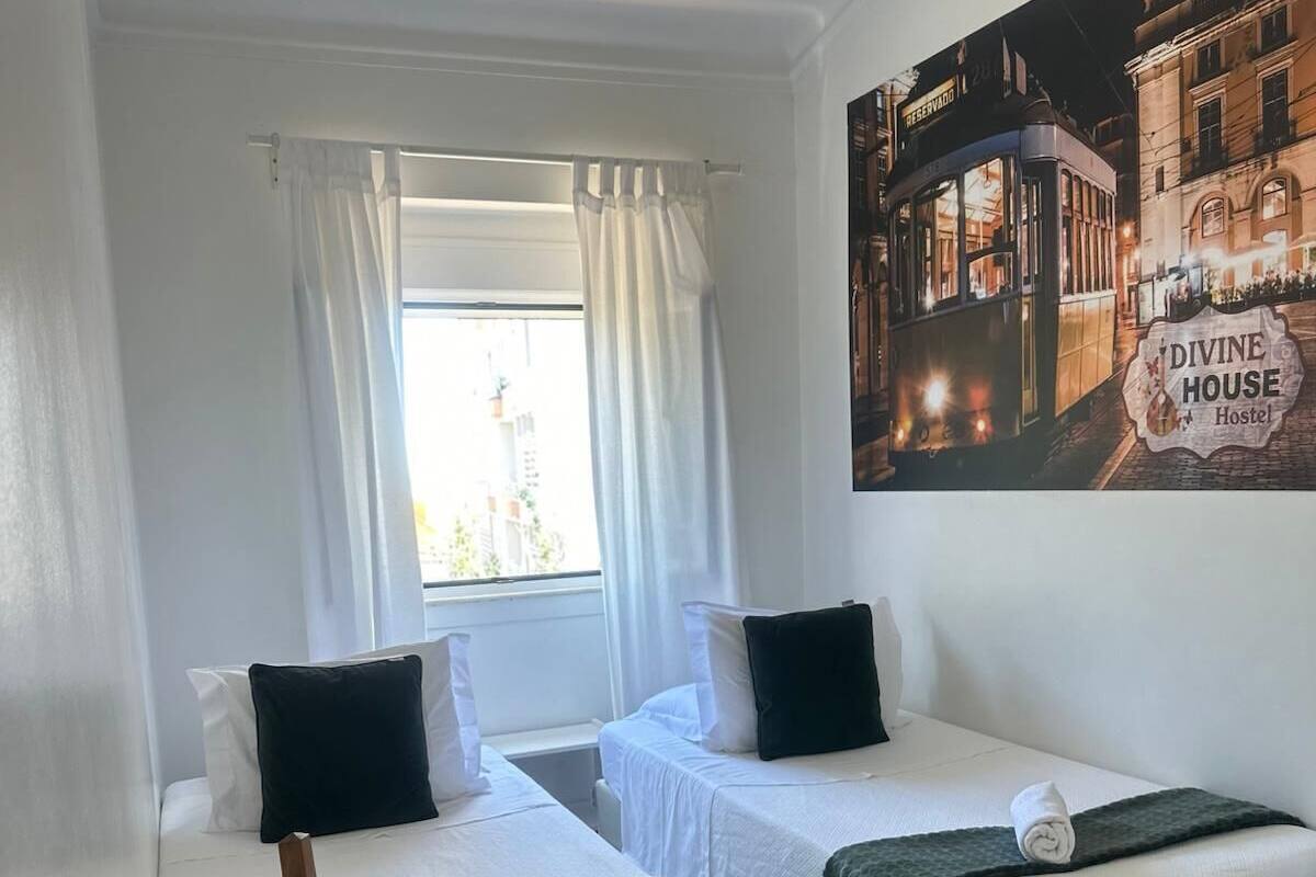Habitación de hotel con dos camas, una silla de madera, una ventana con cortinas y un cartel en la pared de un edificio.