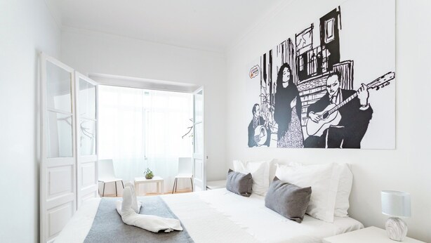 A modern hotel room with a large bed, a bedside table, a nightstand, and a window with a view.