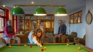 Ett biljardbord med bollar, en klocka på väggen och människor som sitter och spelar.