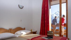 A bedroom with two beds, a laptop on one bed, and a view of a mountain through a sliding door. - 200m from ski slopes, fitness, balcony, parking, tv, ski locker, 42m², Les 2 Alpes (Les Deux Alpes)