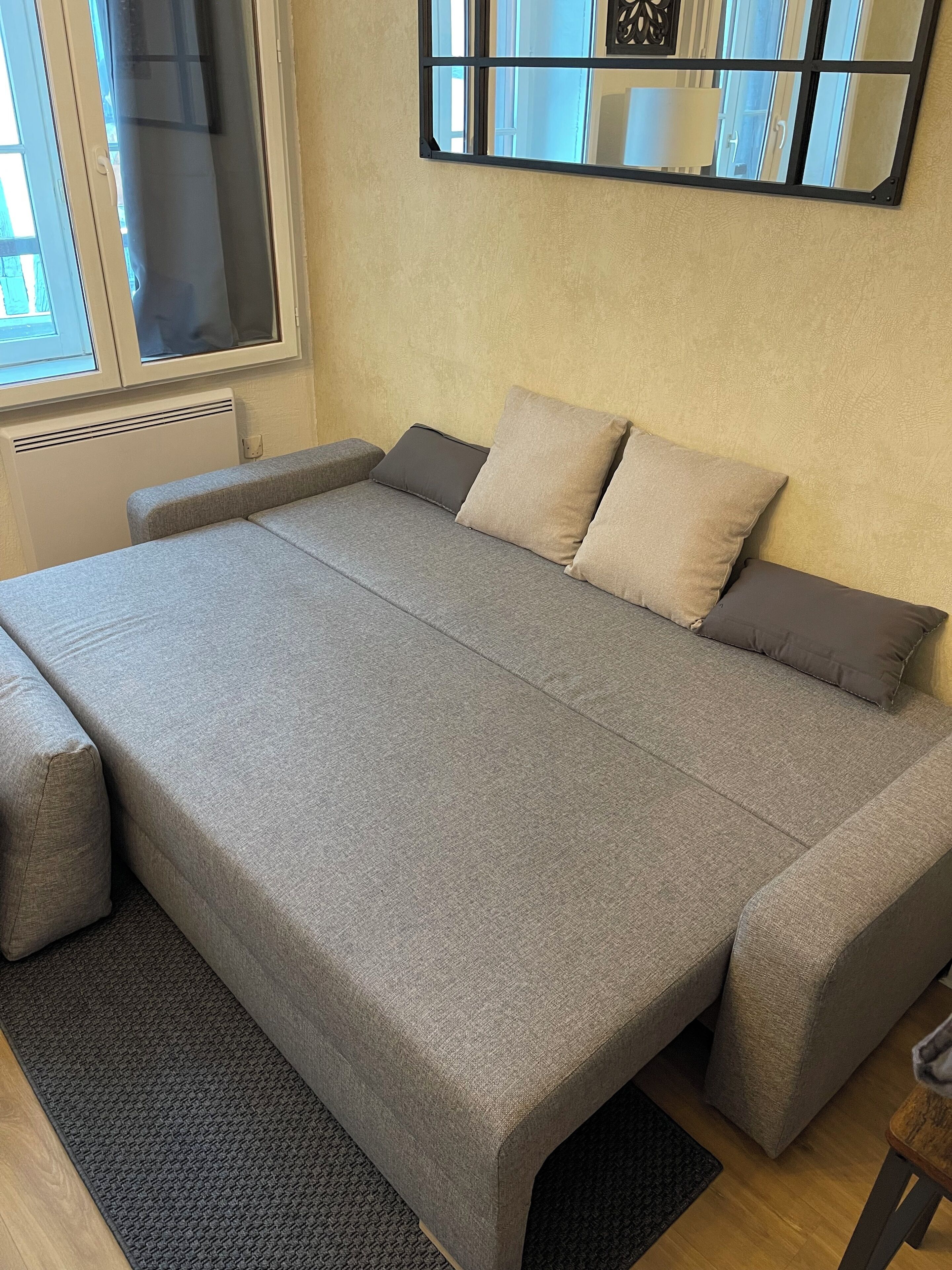 Un dormitorio moderno con una cama grande, una ventana con persianas, un espejo en la pared y un radiador.