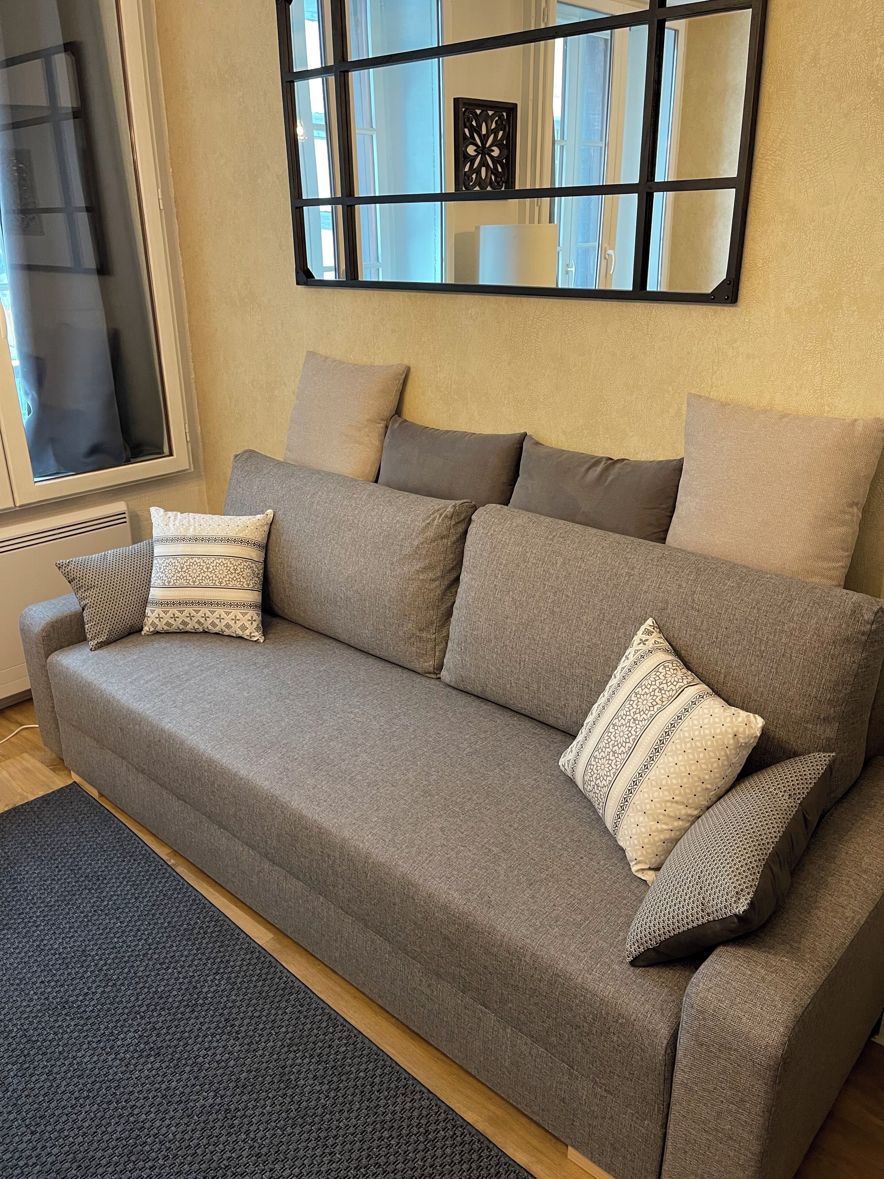 A grey sofa with patterned cushions, a dark rug, and a decorative wall piece.