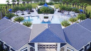 A large building with a central swimming pool, surrounded by palm trees and a lake.