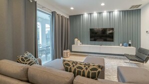 A modern living room with a large flat-screen TV mounted on a wall, a sofa set, and a small coffee table.