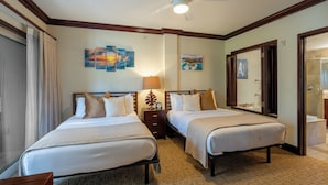 A hotel room with two beds, a ceiling fan, artwork on the walls, and a bathroom visible through an open door.