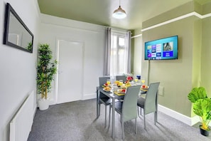 A dining area with a table set for four, a television mounted on the wall, and potted plants. - Central - 2br House - Free Parking - Garden (Coventry)