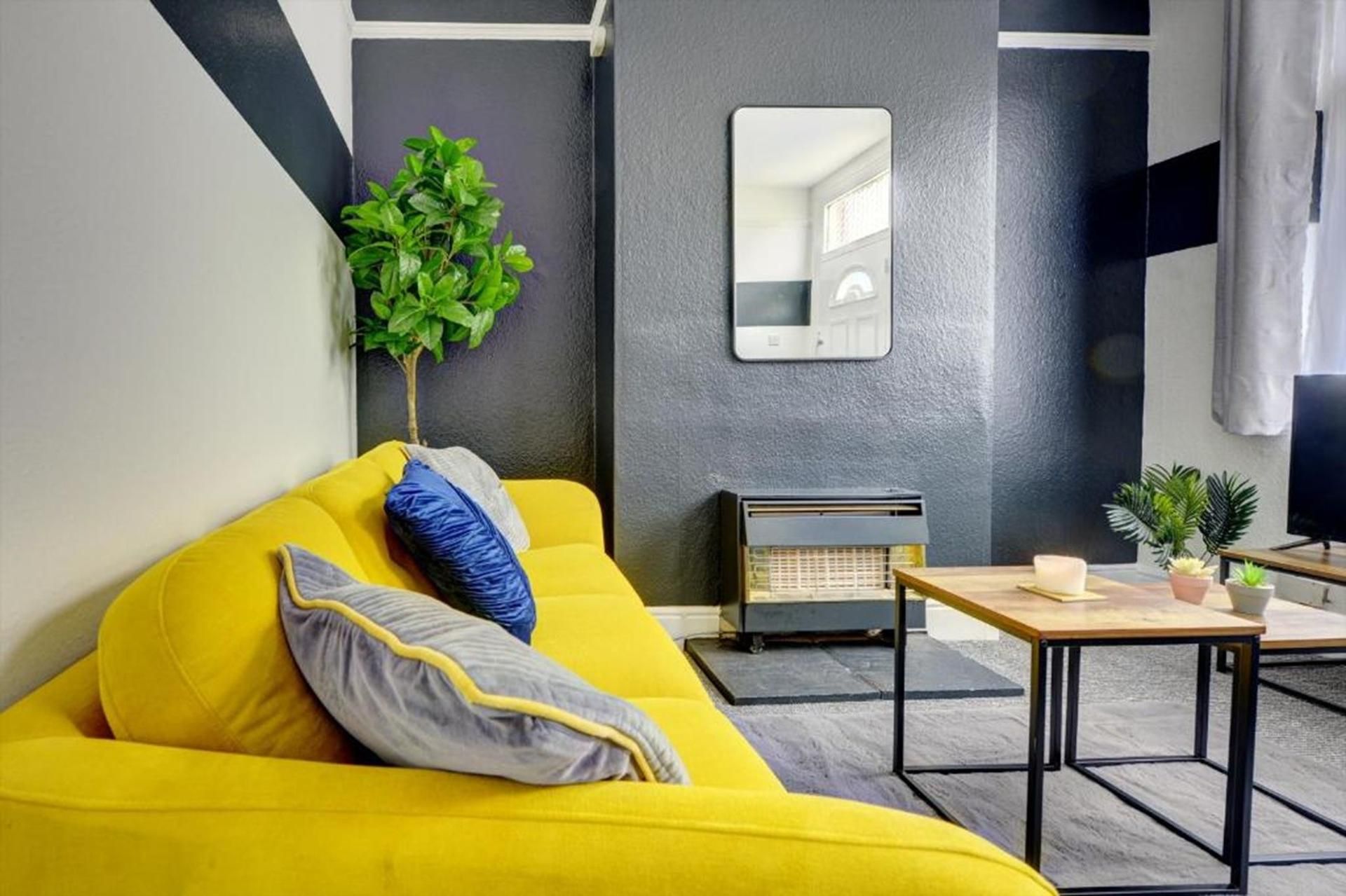 Un salon moderne avec un canapé jaune, une petite table, un radiateur et un miroir accroché au mur.