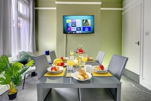 A dining area with a table set for breakfast, a flat-screen TV mounted on the wall, and a potted plant. - Central - 2br House - Free Parking - Garden (Coventry)