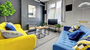 A living room with a yellow sofa, a blue sofa, a TV, and a small table with a plant. - Central - 2br House - Free Parking - Garden (Coventry)