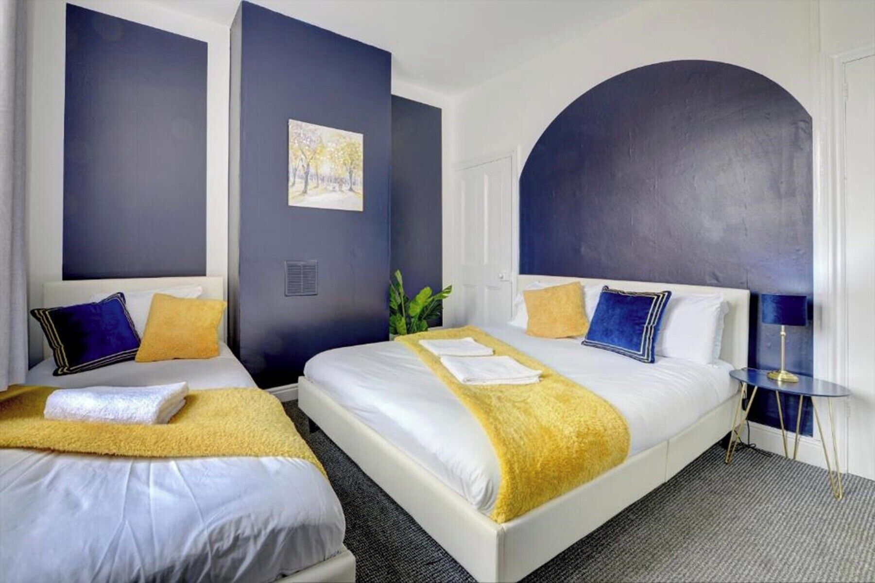 A hotel room with two beds, a large arched window, and a painting on the wall.