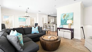 Ein modernes Wohnzimmer mit Ecksofa, Couchtisch aus Holz und Essbereich, im Hintergrund befindet sich eine Küche.