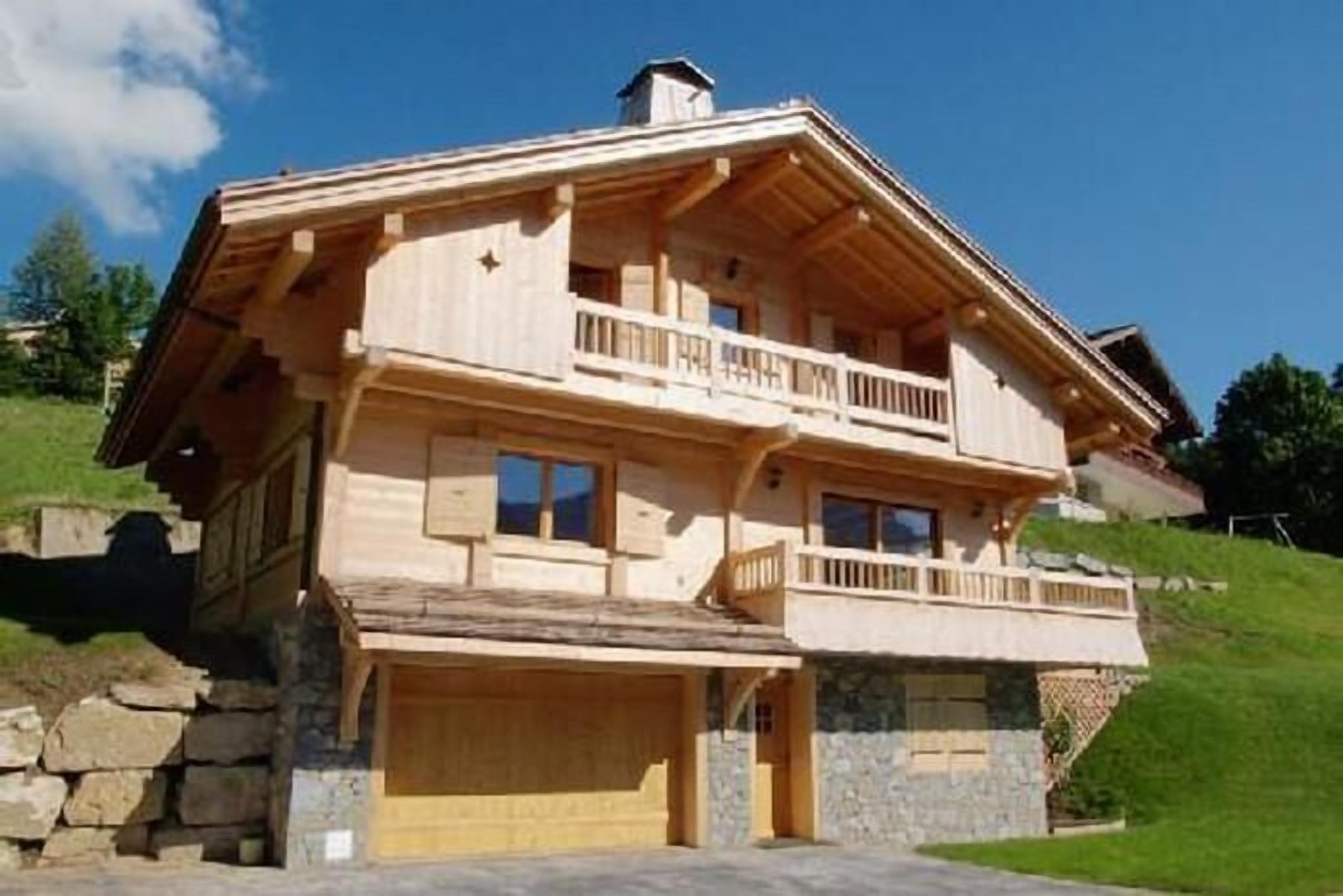 A two-story wooden house with a balcony on the upper floor, a stone foundation, and a garage.