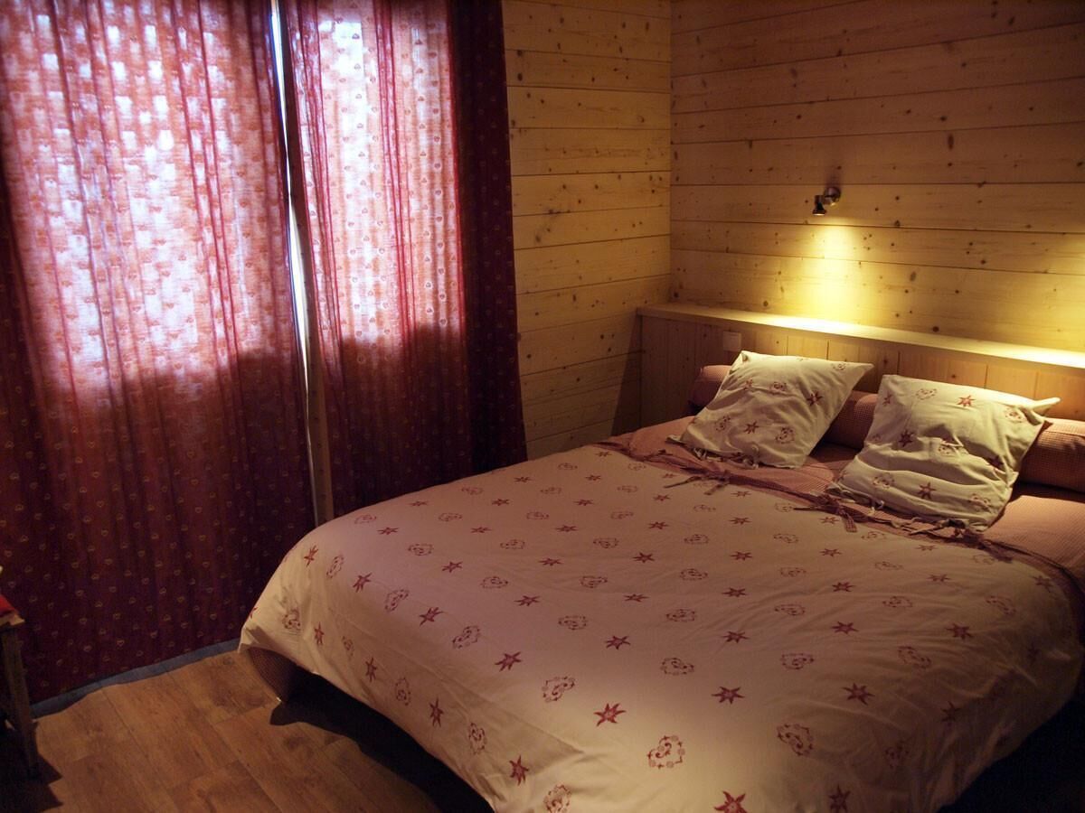 Een slaapkamer met een houten hoofdbord, een bed met een geborduurde spreideken en een nachtkastje met een lamp.