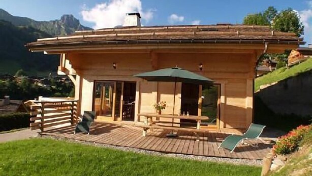 A wooden chalet with a patio, outdoor seating, and a view of mountains. - Chalet, wifi, 100m from ski slopes, hammam, terrace, balcony, fireplace or stove, parking, tv (Le Grand-Bornand)