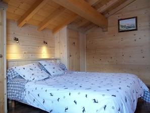 A wooden cabin bedroom with a bed, two bedside lamps, and a framed picture on the wall.
