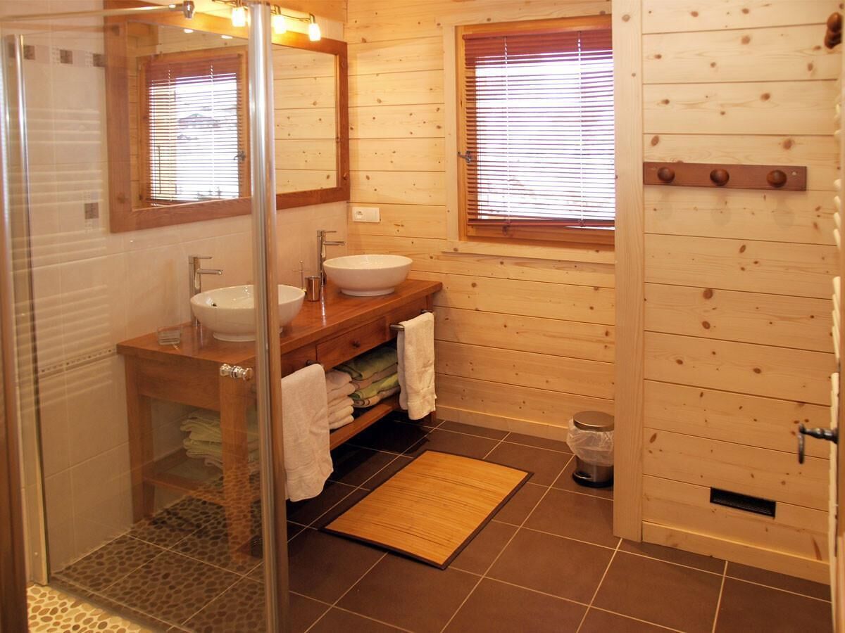 A wooden cabin bathroom with a glass shower enclosure, a wooden vanity with a sink, and a window with blinds.