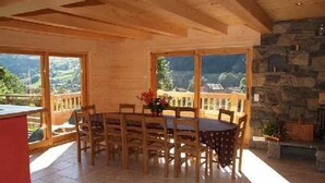A dining area with a round table and chairs, large windows, and a stone wall. - Chalet, wifi, 100m from ski slopes, hammam, terrace, balcony, fireplace or stove, parking, tv (Le Grand-Bornand)