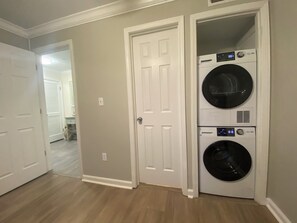 A laundry room with two stacked washers and dryers, a white door, and a hallway leading to another room. - SeaMaster 110: Oceanfront 3 bed 3 bath condo (Murrells Inlet)