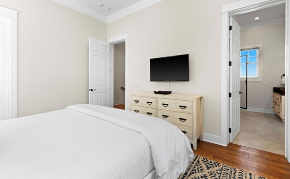 A bedroom with a bed, a dresser, a television, and a door leading to another room.