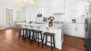 Une cuisine moderne avec des meubles blancs, un grand îlot central doté de tabourets, un réfrigérateur en acier inoxydable et des luminaires suspendus.