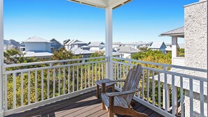 Une terrasse en bois avec une balustrade blanche, une chaise en bois et une vue sur des maisons en arrière-plan.
