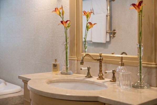 A bathroom with a marble sink, gold faucets, and three vases with flowers.