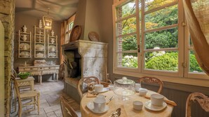 A dining area with a table set for four, surrounded by wooden chairs. A fireplace with a stone mantle is visible, and shelves with dishes and pottery are in the background. - Wisteria Holiday Home (Lonato)