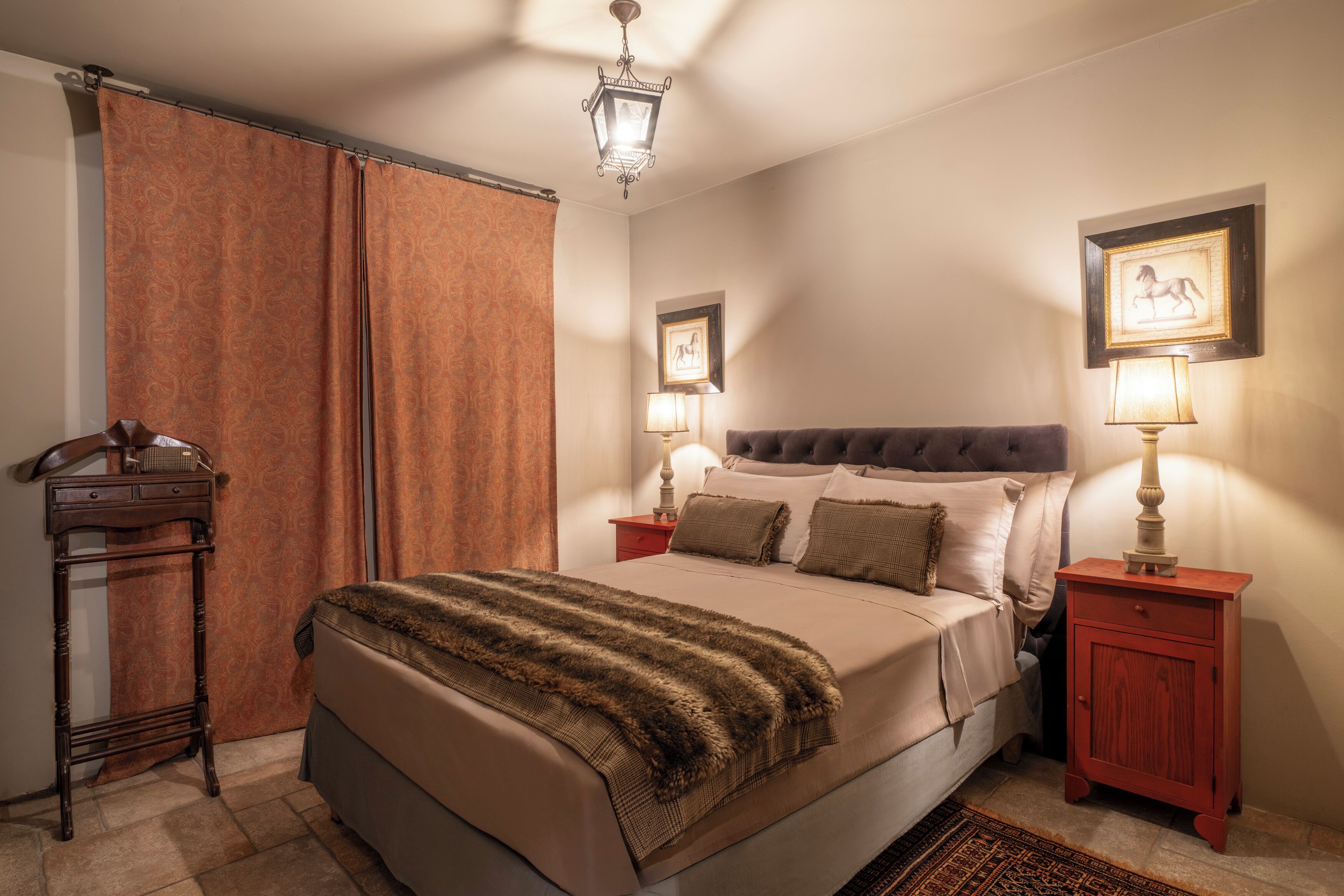 A neatly arranged bedroom with a large bed, two bedside tables with lamps, a wooden nightstand, and a patterned curtain.