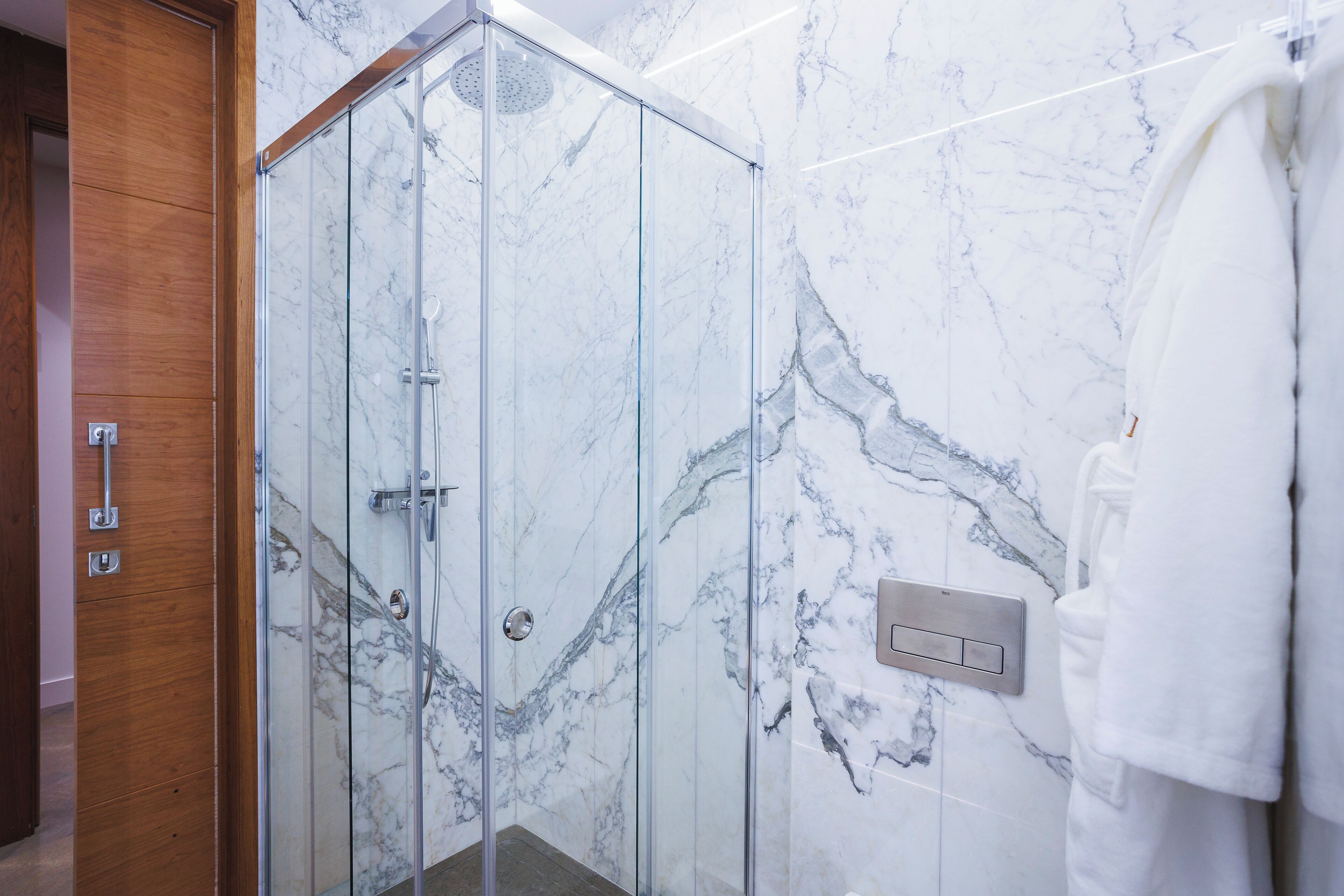 A glass-enclosed shower with a marble wall and a wooden door.