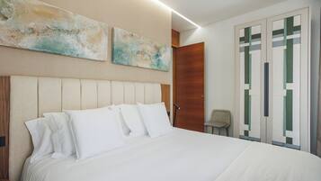 A neatly made bed with white linens and a headboard, a wooden door, and two abstract wall paintings.