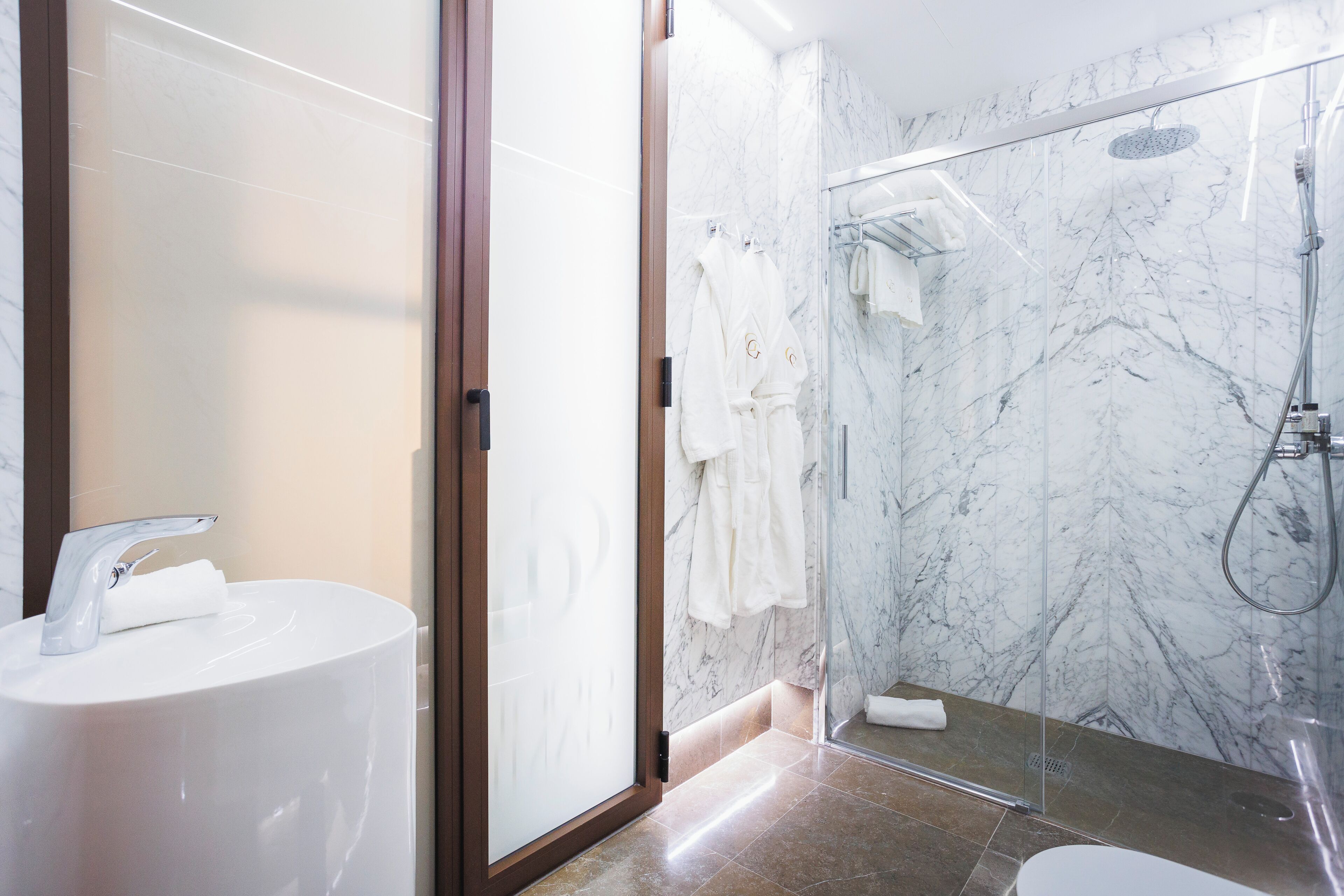 Ein modernes Badezimmer mit einer Duschkabine aus Marmor, einer separaten Toilette und einem weißen Waschbecken.