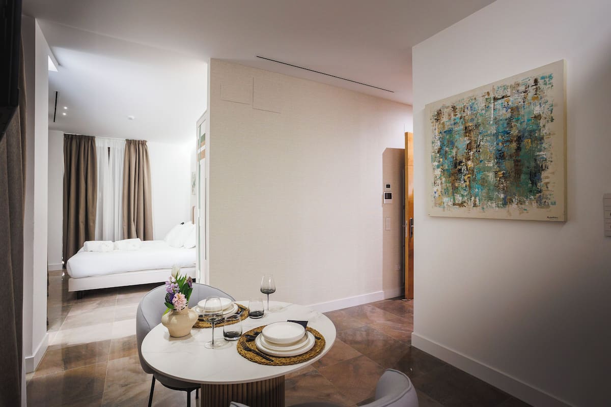 Una habitación de hotel moderna con zona de comedor, cama y un cuadro abstracto grande en la pared.