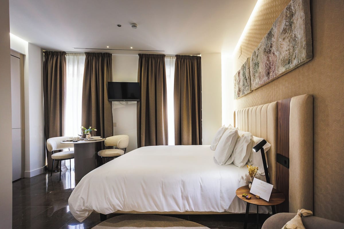 Una habitación de hotel moderna con una cama grande, un escritorio con silla, un televisor de pantalla plana y un cuadro en la pared.