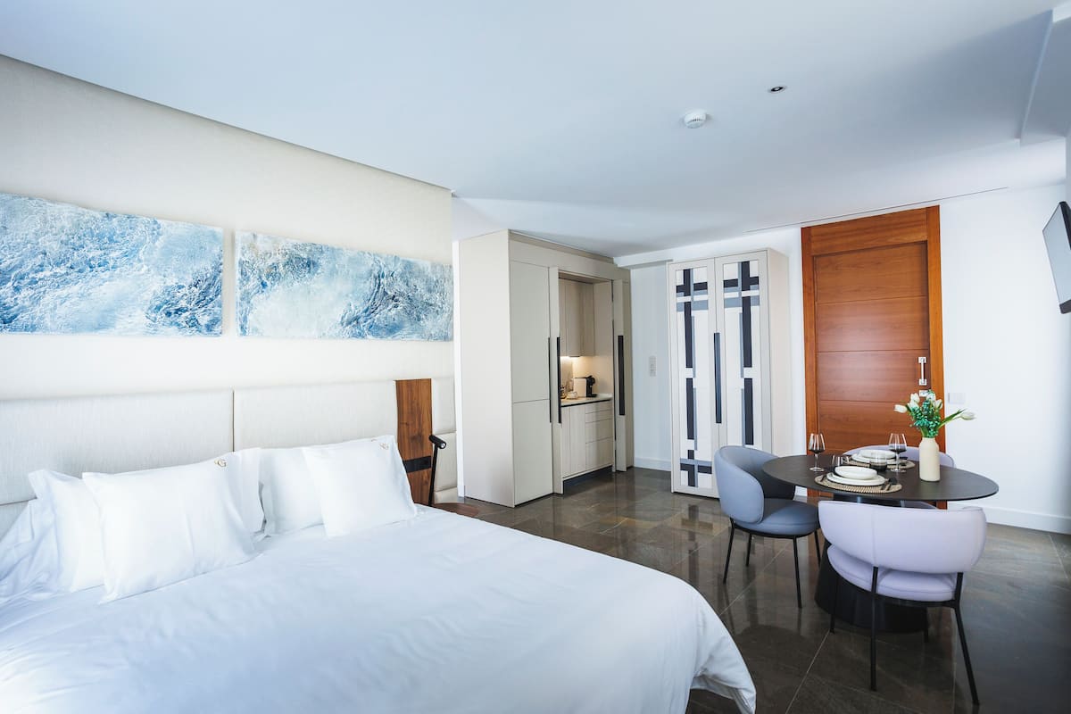 Una habitación de hotel moderna con una cama grande, un área de comedor con mesa y sillas, y una cocina.