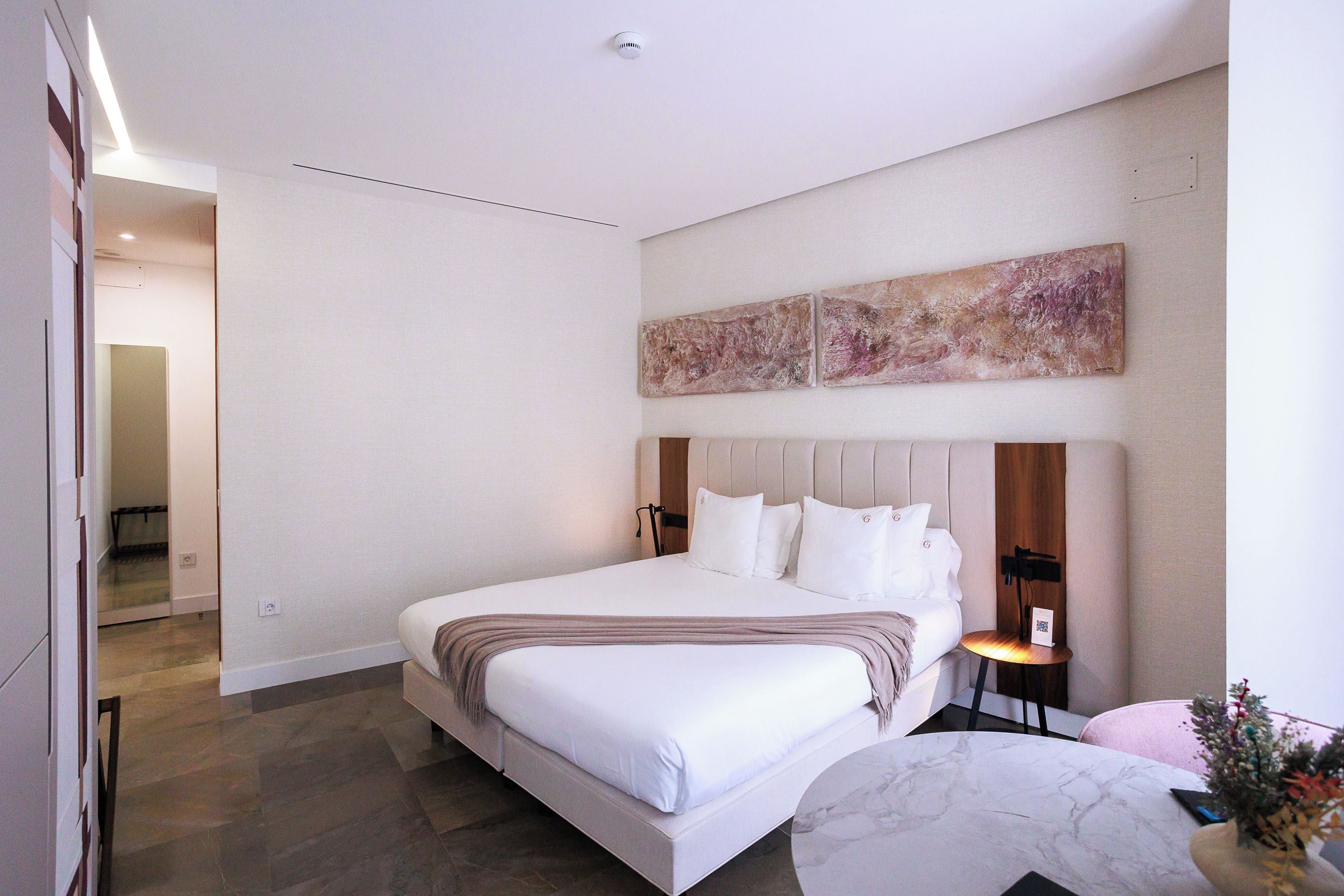 Una habitación de hotel moderna con una cama grande, una mesita de mármol y una obra de arte colgada en la pared.