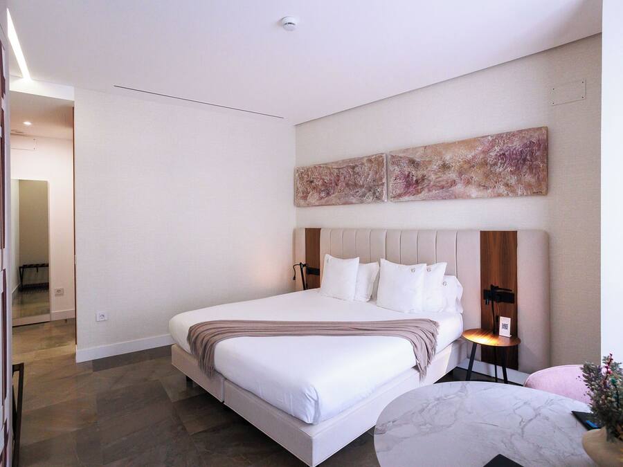 A modern hotel room with a large bed, a marble side table, and a wall-mounted artwork.