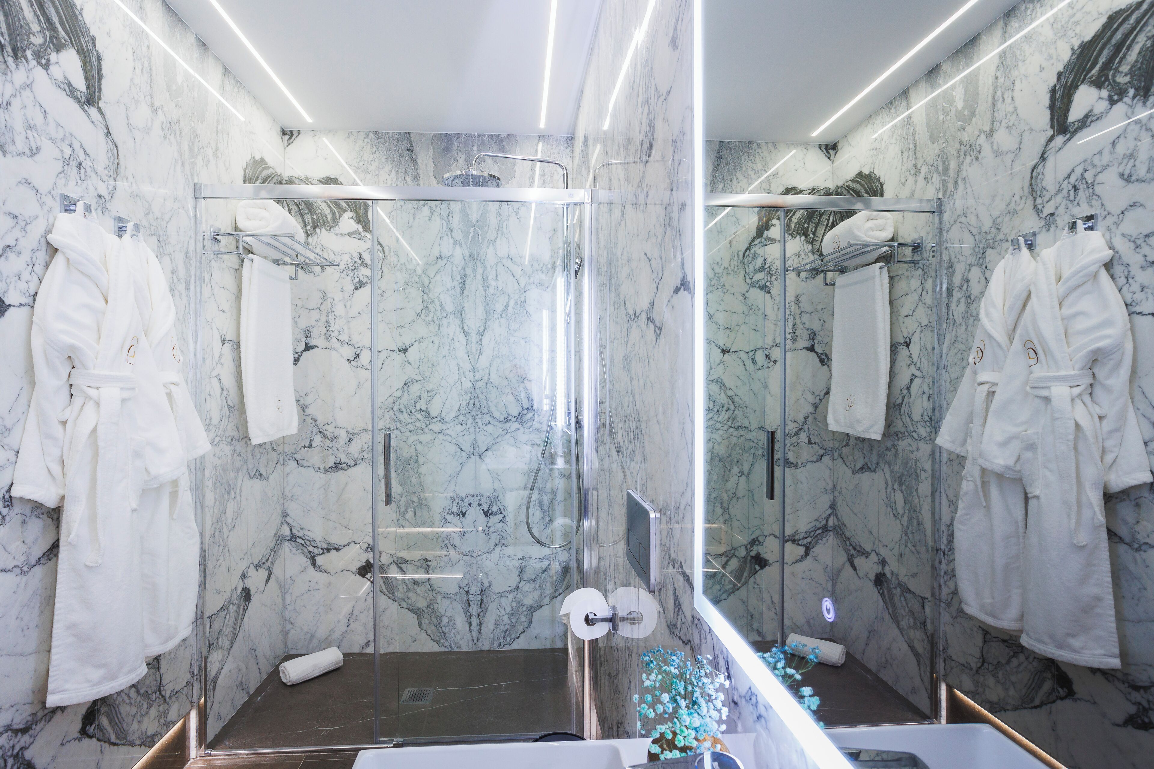 Ein modernes Badezimmer mit Marmorwänden, einer Glaskabine für die Dusche und mehreren weißen Handtüchern und Bademänteln.