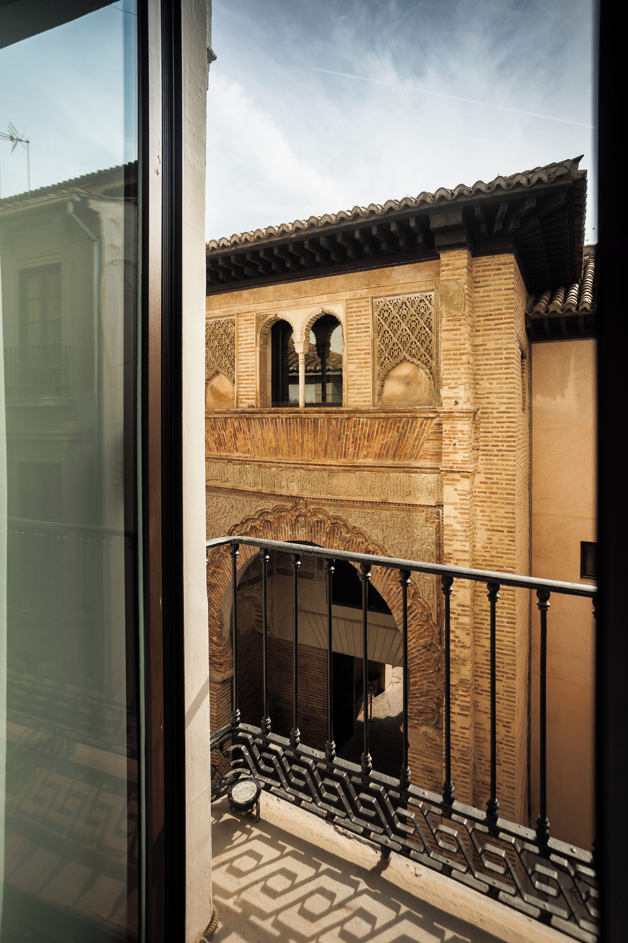 A balcony with a wrought iron railing overlooking a courtyard with a brick wall and decorative arches.