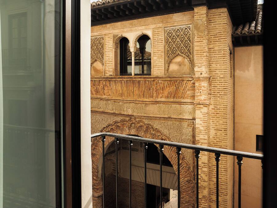 Un balcón con barandilla de hierro forjado que da a un patio con pared de ladrillo y arcos decorativos.