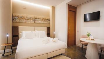 A modern hotel room with a large bed, a round table, a TV, and artwork on the wall.