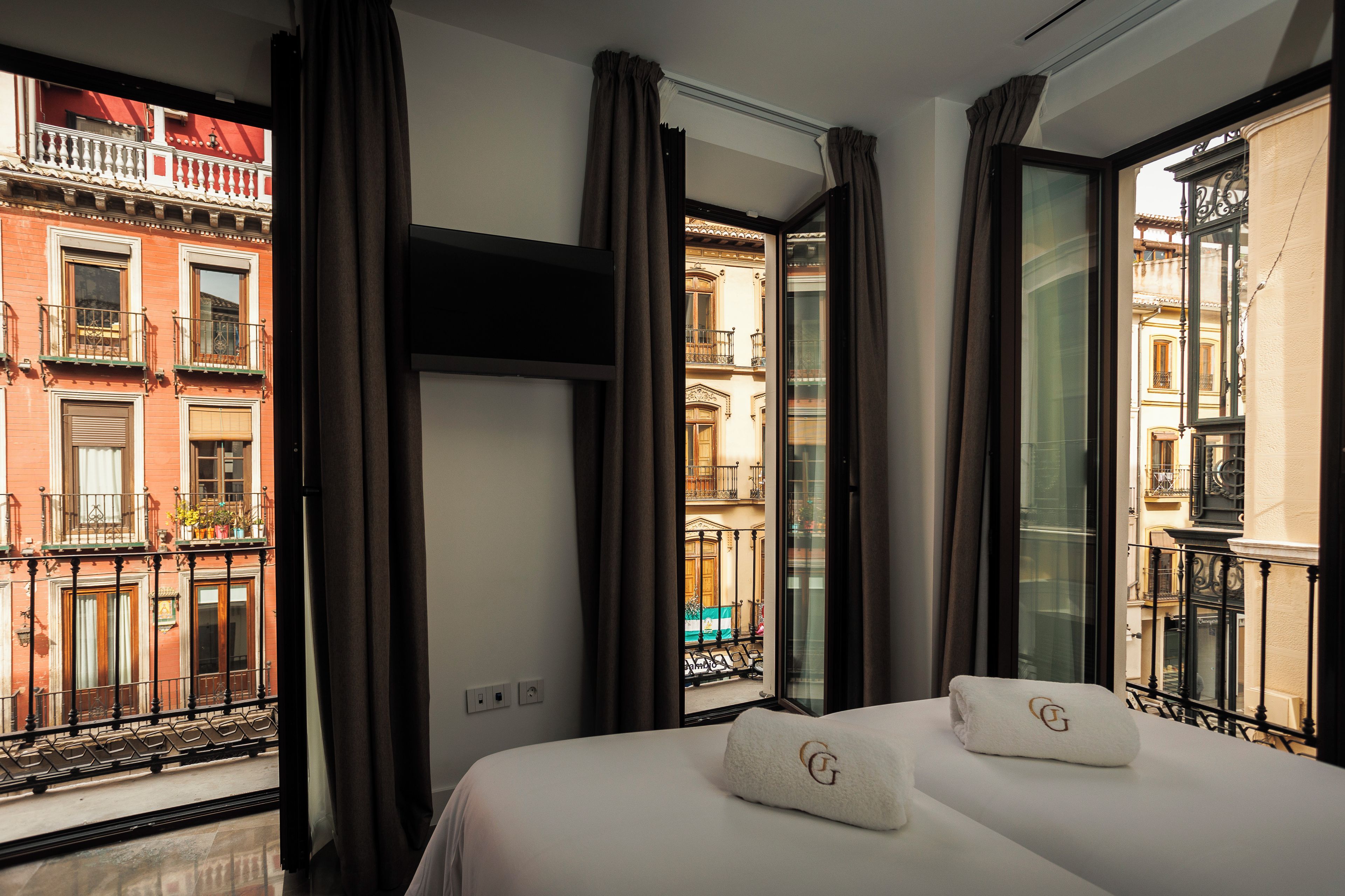 Une chambre d’hôtel avec un lit, deux oreillers, une télévision et de grandes fenêtres équipées de rideaux.