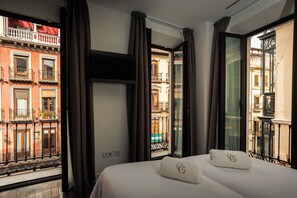 Habitación de hotel con cama, dos almohadas, televisor y ventanas grandes con cortinas.