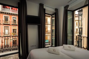 A hotel room with a bed, two pillows, a TV, and large windows with curtains.