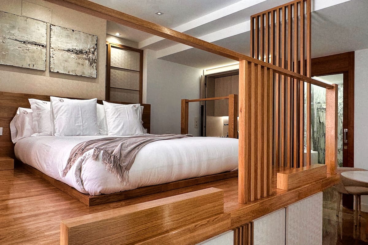 Un dormitorio moderno con una cama grande, cabecera de madera y vistas al baño.
