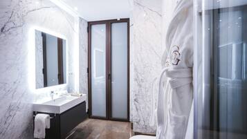 Un baño moderno con pared de mármol, un espejo grande, un lavamanos blanco y un box de ducha de vidrio.