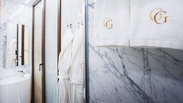 A modern bathroom with a marble sink, glass shower enclosure, and white towels with a monogram.